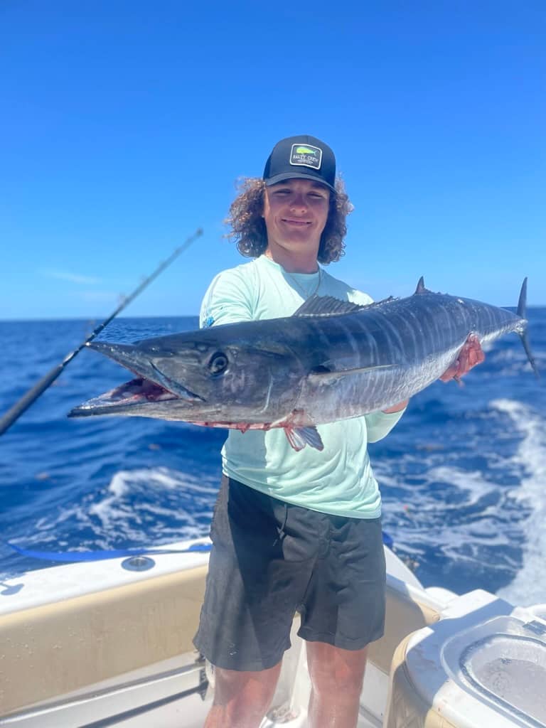 Teenager standing on boat out on the water holding up Wahoo catch
